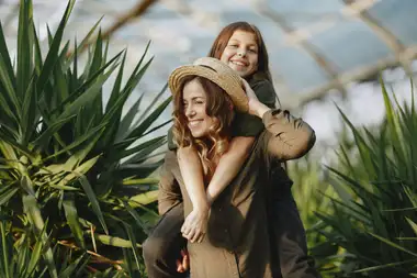 Mother giving her daughter a piggyback ride in a sunlit greenhouse